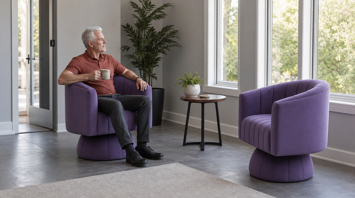 “Man holding a mug in one of two purple swivel chairs arranged beside a small table in a sunlit room.”