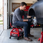 Mechanic seated on the yellow rolling stool performing a front brake job in a home garage