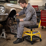 Mechanic seated on the yellow rolling stool performing a front brake job in a home garage