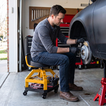 Mechanic seated on the yellow rolling stool performing a front brake job in a home garage