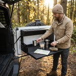 Person using the fold-down tailgate table at an open vehicle rear door outdoors