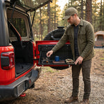 Person using the fold-down tailgate table at an open vehicle rear door outdoors
