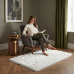Ultra-soft faux sheepskin area rug in white placed in living room beside armchair