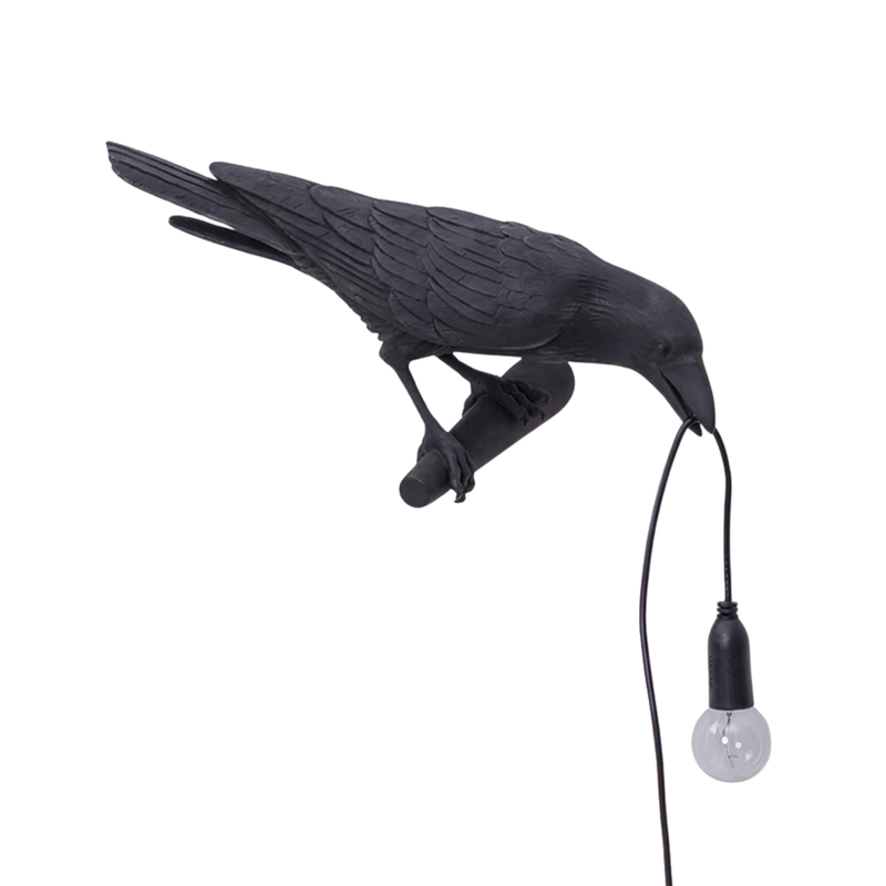 Black gothic raven lamp holding a hanging cord with a lit filament bulb on a white background