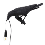Black gothic raven lamp holding a hanging cord with a lit filament bulb on a white background