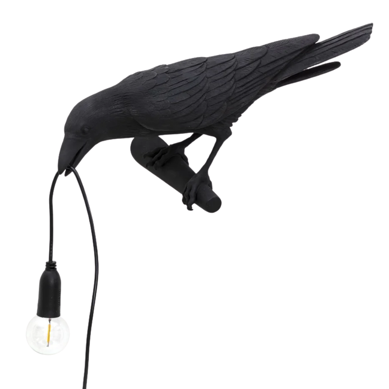 Black gothic raven lamp holding a hanging cord with a lit filament bulb on a white background