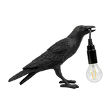 Black gothic raven lamp holding a hanging cord with a lit filament bulb on a white background