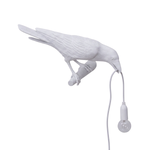 Black gothic raven lamp holding a hanging cord with a lit filament bulb on a white background