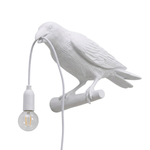 Black gothic raven lamp holding a hanging cord with a lit filament bulb on a white background