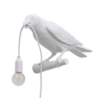 Black gothic raven lamp holding a hanging cord with a lit filament bulb on a white background