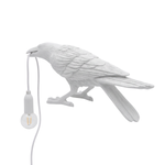 Black gothic raven lamp holding a hanging cord with a lit filament bulb on a white background