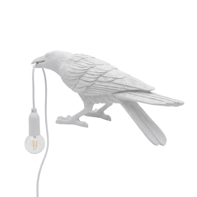 Black gothic raven lamp holding a hanging cord with a lit filament bulb on a white background