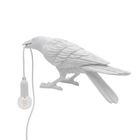 Black gothic raven lamp holding a hanging cord with a lit filament bulb on a white background