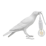 Black gothic raven lamp holding a hanging cord with a lit filament bulb on a white background