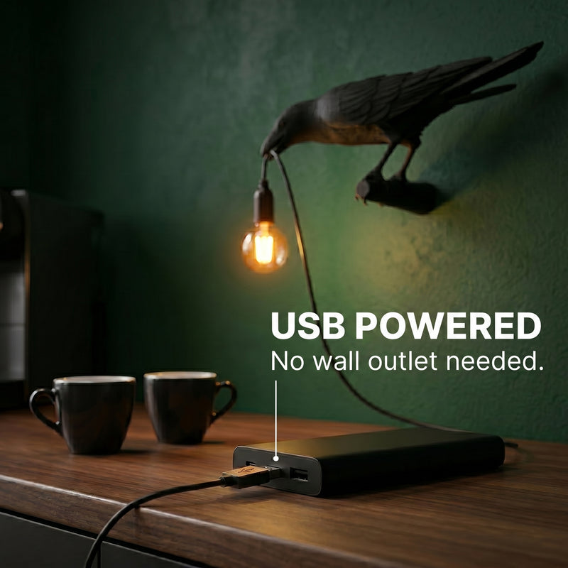 Black raven lamp on a wood desk connected to a USB power bank among vintage books and a magnifying glass