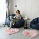 Pink heart shaped faux fur rug on a wood bedroom floor beside a bed