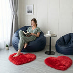 Pink heart shaped faux fur rug on a wood bedroom floor beside a bed