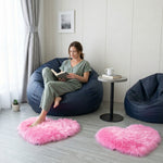 Pink heart shaped faux fur rug on a wood bedroom floor beside a bed