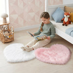 Pink heart shaped faux fur rug on a wood bedroom floor beside a bed