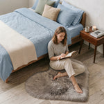 Pink heart shaped faux fur rug on a wood bedroom floor beside a bed