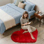 Pink heart shaped faux fur rug on a wood bedroom floor beside a bed