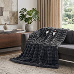 White faux rabbit fur heated blanket with bubble texture draped over a grey sofa in a modern living room