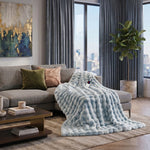 White faux rabbit fur heated blanket with bubble texture draped over a grey sofa in a modern living room
