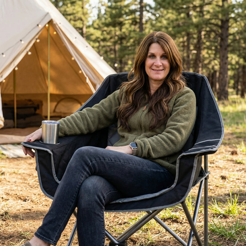 Woman relaxing in a black oversized folding camping chair on a beach with a drink in the cup holder