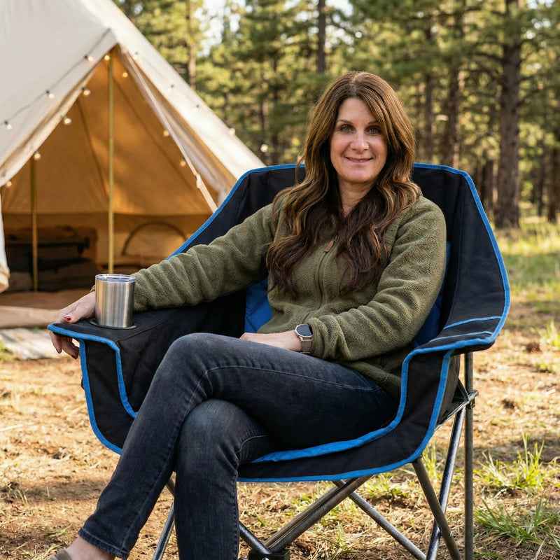 Woman relaxing in a black oversized folding camping chair on a beach with a drink in the cup holder