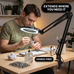 Man using a clamp-mounted LED magnifying lamp to hand-paint a miniature figure at a hobby desk