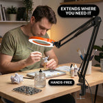 Man using a clamp-mounted LED magnifying lamp to hand-paint a miniature figure at a hobby desk