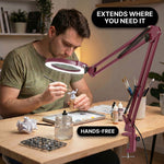 Man using a clamp-mounted LED magnifying lamp to hand-paint a miniature figure at a hobby desk