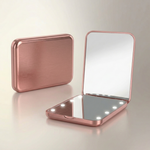 LED travel makeup mirror in pink, shown closed and open with LED lights on