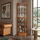 Oak lighted corner curio cabinet displaying crystal and glassware in a living-room corner