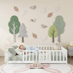Toddler resting on a natural Montessori floor bed with fence in a forest-themed nursery