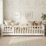 Toddler resting on a natural Montessori floor bed with fence in a forest-themed nursery