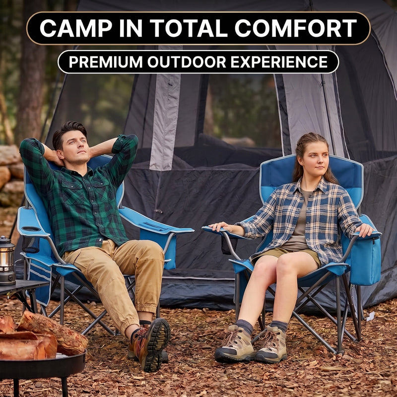 A man and woman relaxing in a matching pair of oversized camping chairs at a wooded campsite with tents and a campfire
