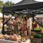 People gathered under a khaki pop-up gazebo canopy at an outdoor garden party with tables of food and flowers
