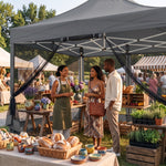 People gathered under a khaki pop-up gazebo canopy at an outdoor garden party with tables of food and flowers