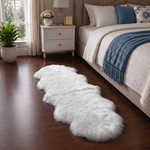Real sheepskin rug in tan placed beside a bed on dark hardwood floor in a bedroom setting