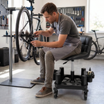 Man sitting on a red rolling garage stool holding a spark plug in a home garage