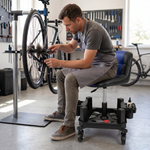 Man sitting on a red rolling garage stool holding a spark plug in a home garage