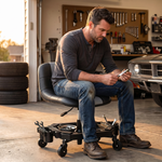 Man sitting on a red rolling garage stool holding a spark plug in a home garage