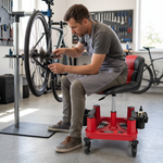 Man sitting on a red rolling garage stool holding a spark plug in a home garage