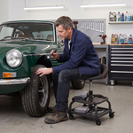 Mechanic sitting on a yellow rolling mechanic stool while working on a car wheel in a garage
