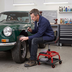 Mechanic sitting on a yellow rolling mechanic stool while working on a car wheel in a garage