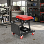 Red and black padded rolling mechanic stool with a divided tool tray and five casters in a garage
