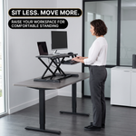 Woman standing at a raised sit-to-stand desk converter with a monitor and laptop