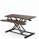 Black standing desk converter shown raised to standing height with keyboard tray