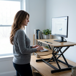 Woman standing at a black standing desk converter with dual monitors in a modern office